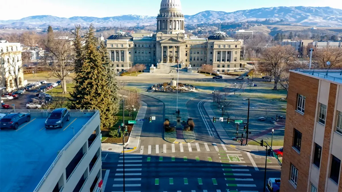 Traffic-dominated roadway and intersection in front of the Idaho State Capitol, with wide lanes, crosswalks, and minimal pedestrian gathering space.