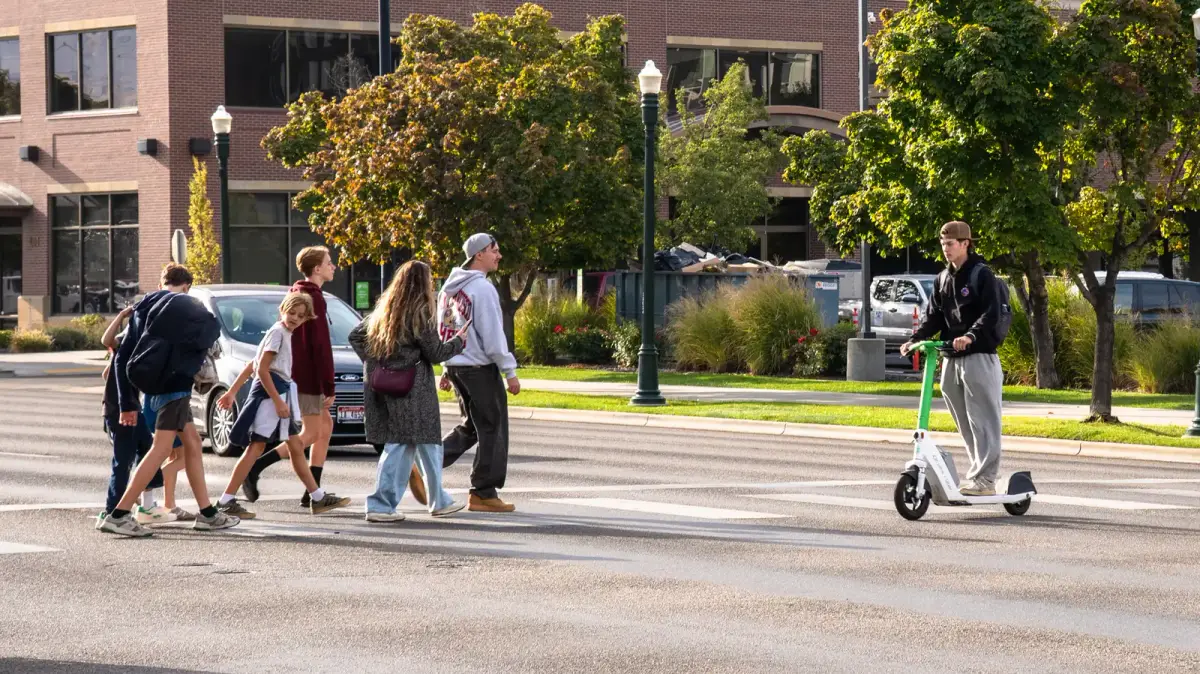 Young people walking across a Boise street while another person rides an electric scooter.