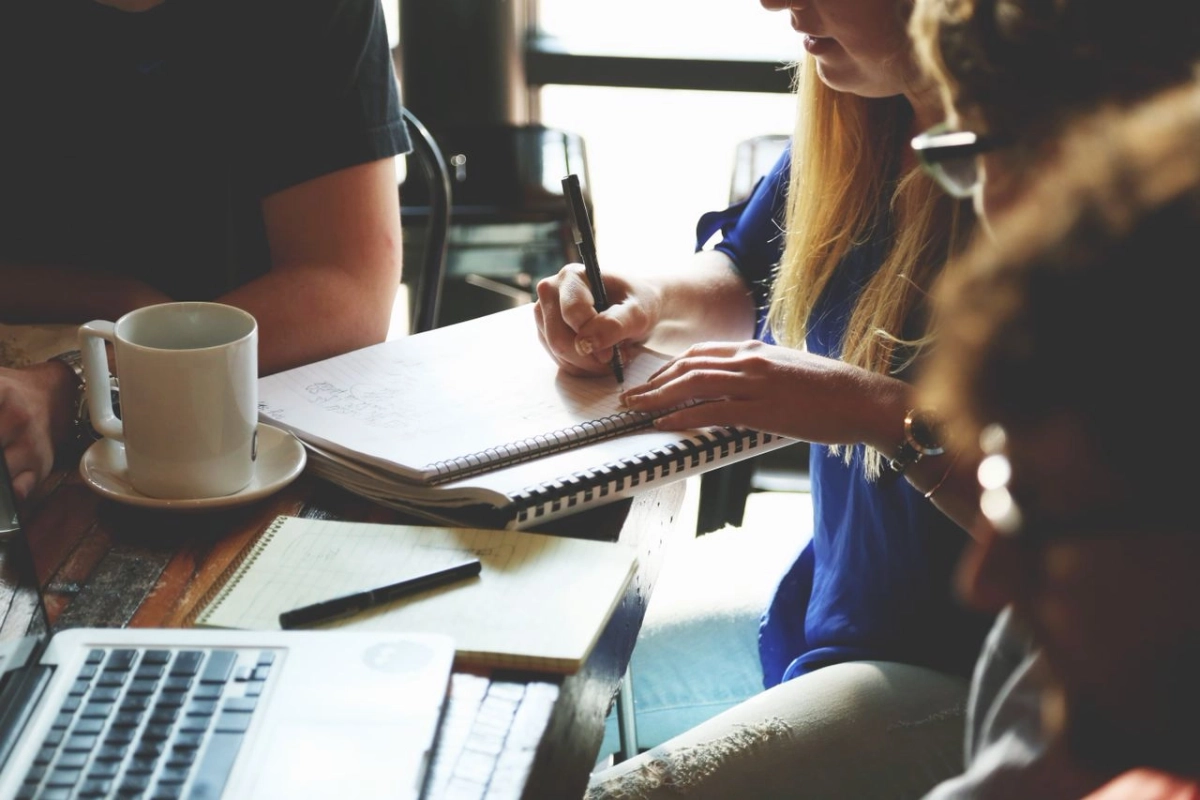 People collaborating around a table with notebooks, coffee, and a laptop during a working session.