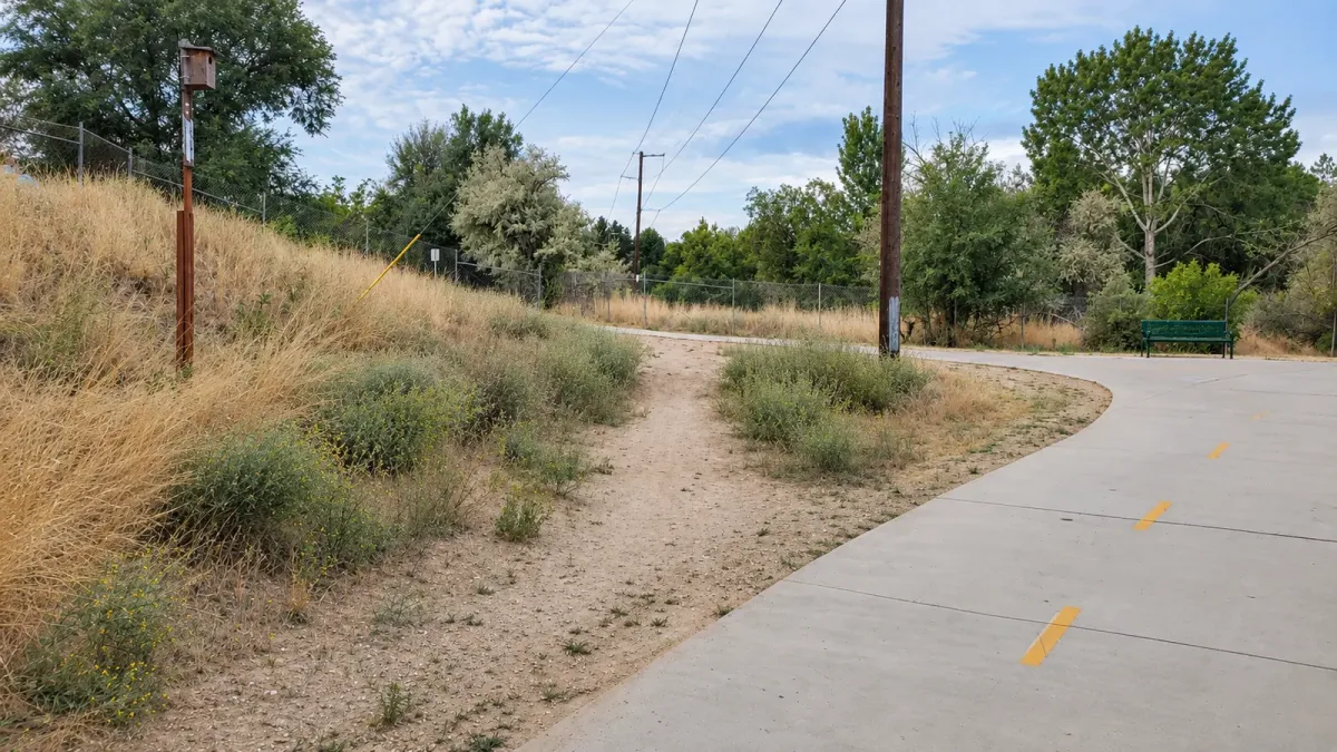 A worn dirt shortcut runs beside a curving paved path at Rotary Park in Boise.