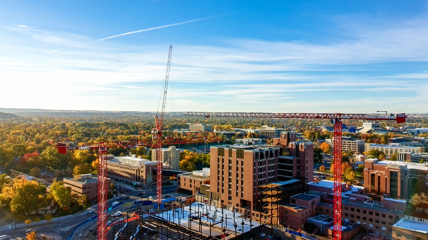 Early-morning aerial view of downtown Boise with construction cranes and an unfinished building frame rising above tree-lined neighborhoods.