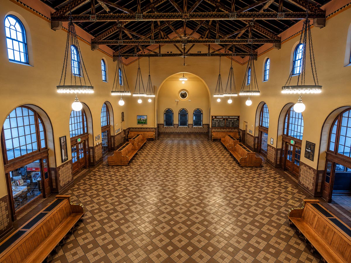 Historic interior of the Boise Depot, with arched windows, wood benches, hanging lights, and a wide tiled hall arranged as a dignified civic room.