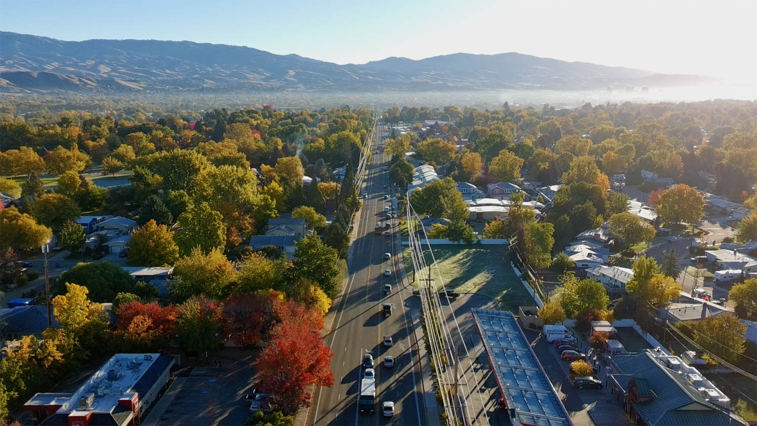 A high-altitude drone view of a straight Boise arterial road stretching toward a hazy mountain horizon, representing civic direction and orientation.