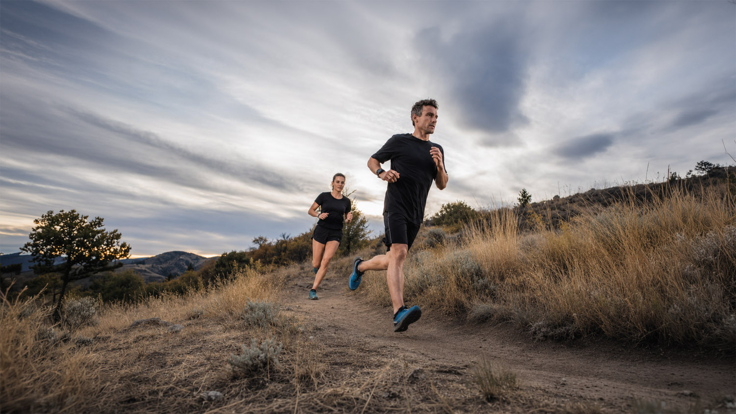 Two runners move along a dry foothills trail under a wide sky, suggesting effort, place, and the ritual of moving through landscape.