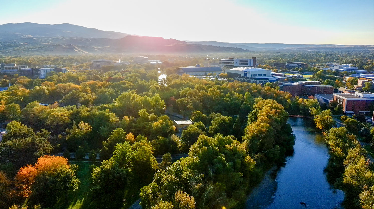 Aerial view of Julia Davis Park’s tree canopy along the Boise River, with downtown Boise and surrounding foothills in the background.