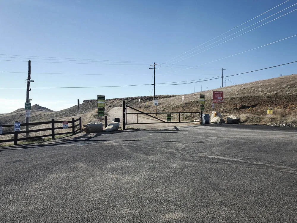 The gated approach to Table Rock with multiple signs, overhead lines, and a gravel road beyond