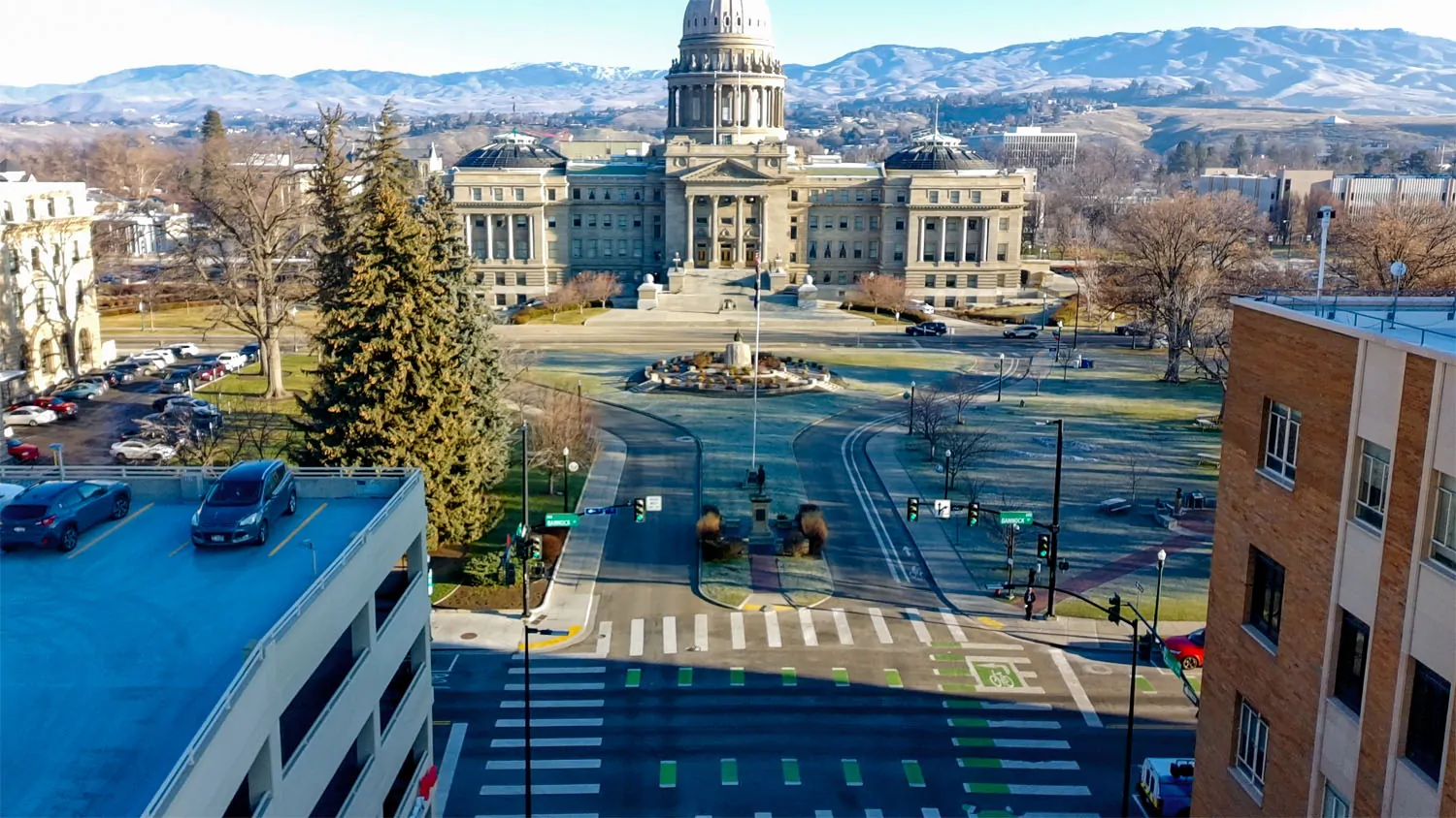 Traffic-dominated roadway and intersection in front of the Idaho State Capitol, with wide lanes, crosswalks, and minimal pedestrian gathering space.